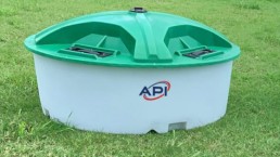 A white and green plastic tank with a rounded base and a green lid sits on a grass lawn, ready for use in agriculture. The tank proudly displays the 