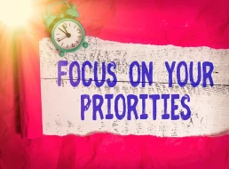 A brightly lit image with a red crumpled paper background features an old-fashioned blue alarm clock and a white wooden sign with large blue text that reads, 